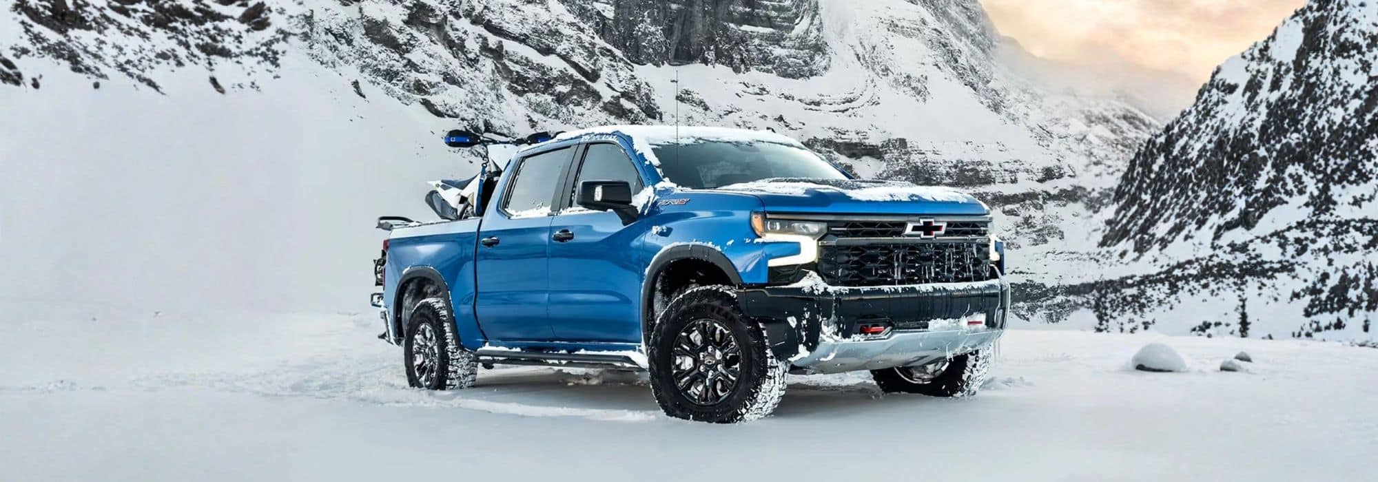 Blue pickup truck in snowy mountain landscape, equipped with roof gear.