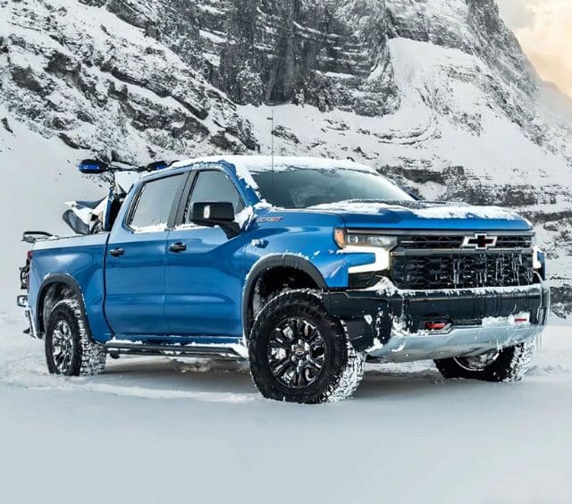Blue Chevrolet truck parked in a snowy mountainous landscape, showcasing winter capability.