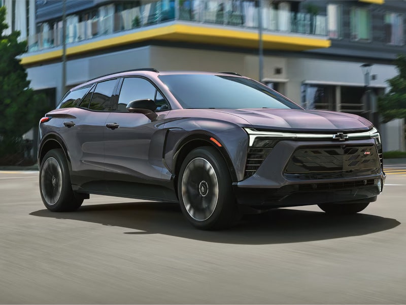 A sleek, modern SUV driving in an urban setting, showcasing its design and glossy finish.
