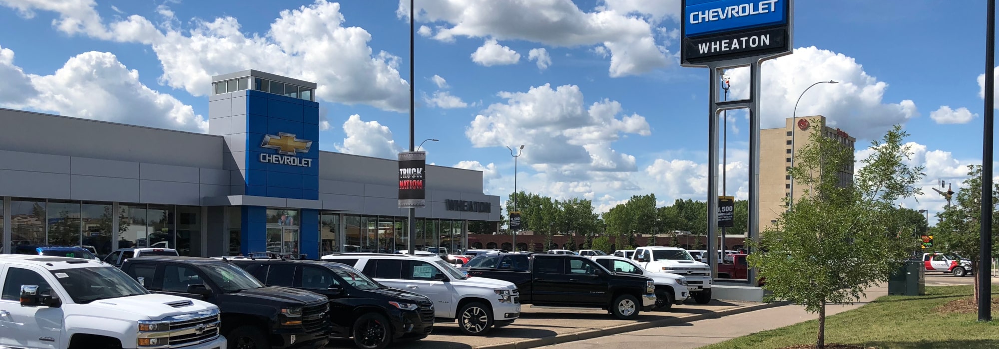 Chevrolet Wheaton dealership with cars parked outside under a blue sky with clouds.