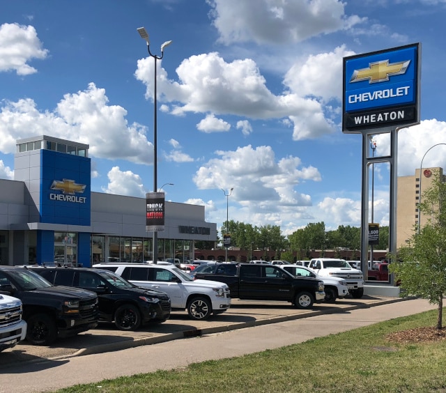 Chevrolet dealership exterior with parked cars and signage under a blue sky.