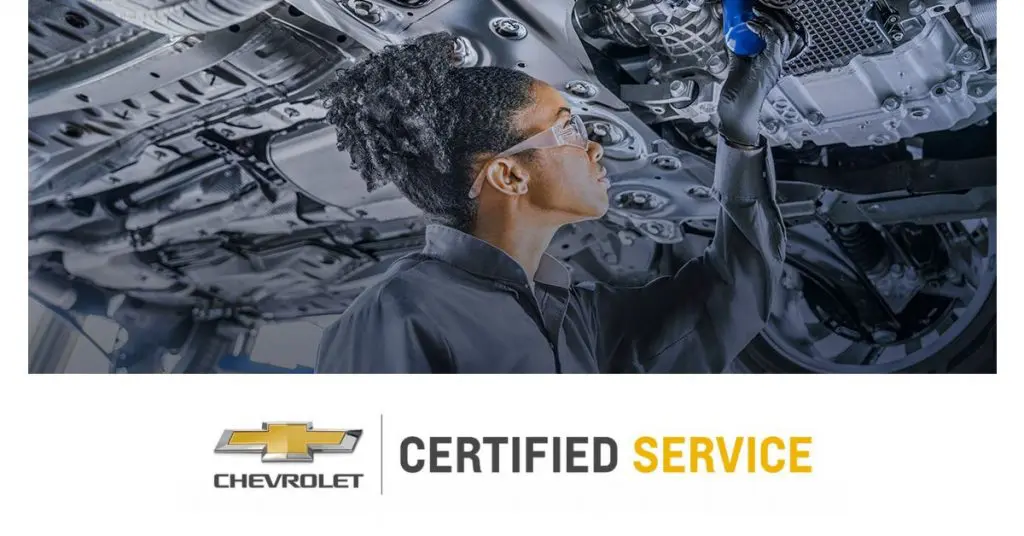 Mechanic performs inspection under car; Chevrolet Certified Service logo below.