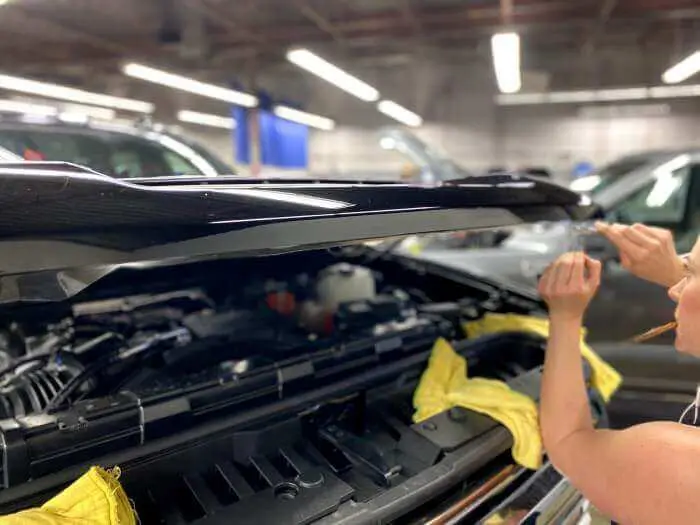 Mechanic working on a car engine in a garage, with hood open and tools in hand.