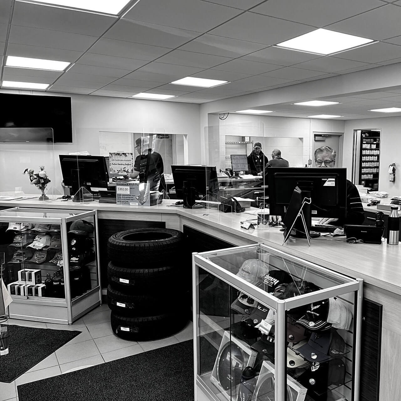Auto service center interior with staff at computers, display shelves with hats, and stacked tires.