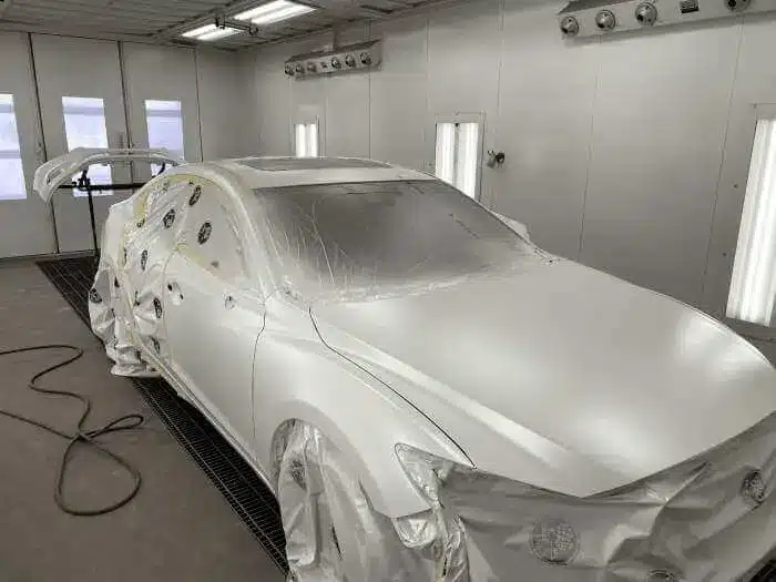 Car in a paint booth covered for spraying, with visible hanging lights and equipment.