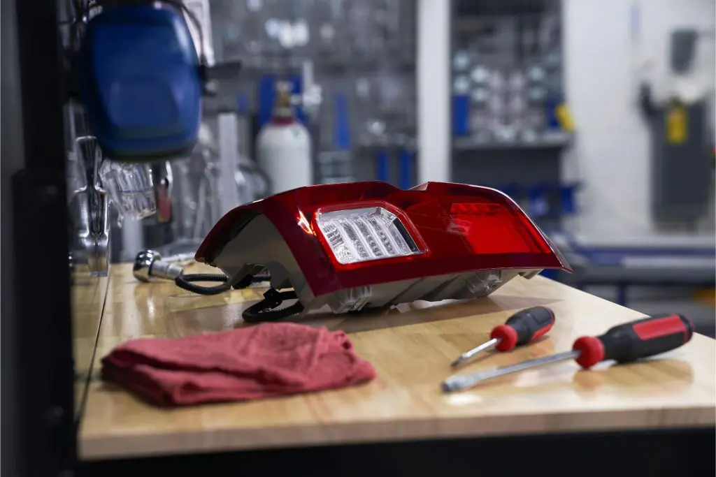 Car tail light on a workbench with red cloth and screwdrivers, automotive repair setting.