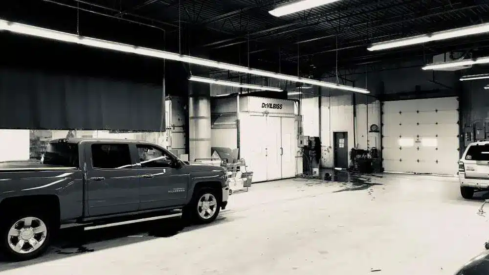 Garage interior with vehicles and equipment, featuring a large DeVILBISS spray booth in the center.
