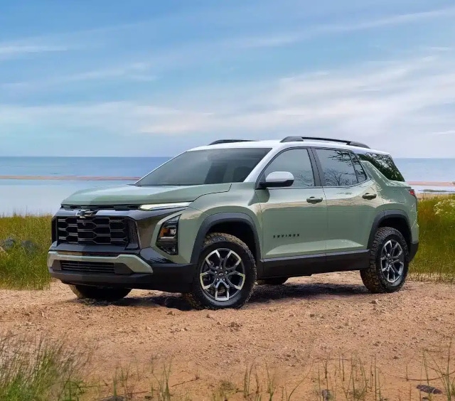 Green SUV parked on sandy terrain near a beach, under a clear blue sky.