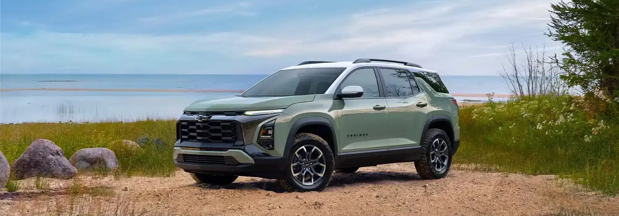 Green SUV parked by a scenic lakeside with rocks and greenery in the foreground.