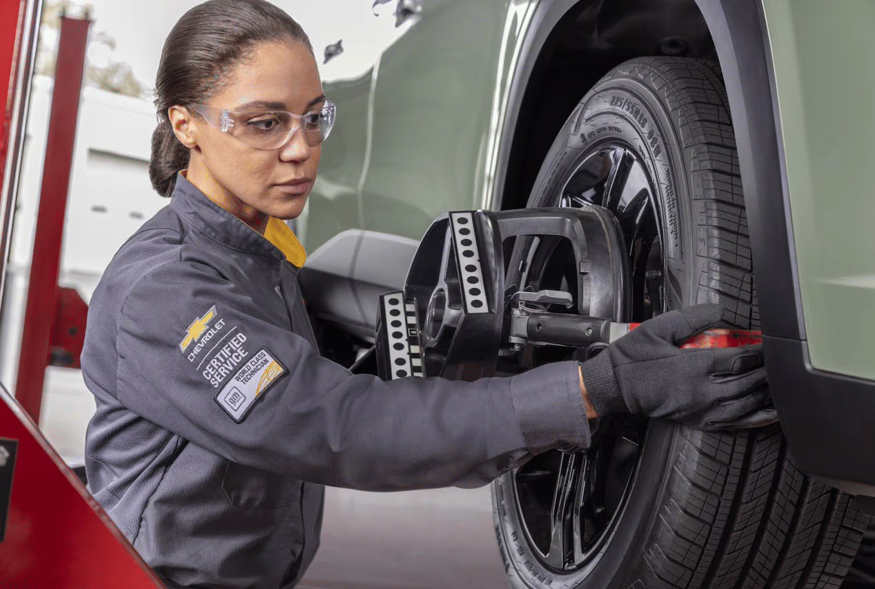 Mechanic adjusting wheel alignment on a car, wearing protective gear and a certified service uniform.
