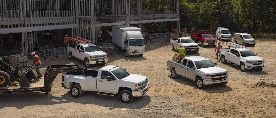 Construction site with multiple white trucks and workers near a building scaffolding.