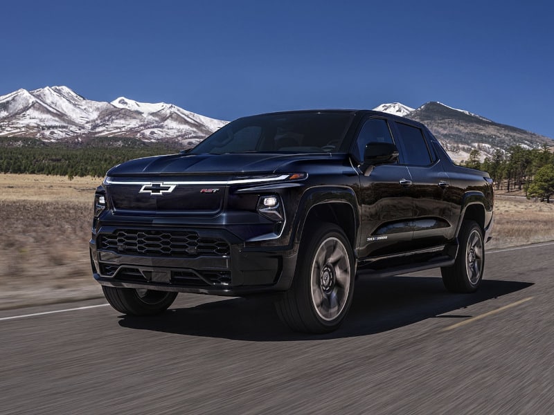Black Chevrolet pickup truck driving on a road with snowy mountains in the background.