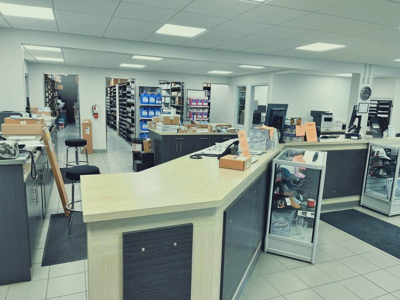 Spacious pharmacy counter with shelves of products, computers, and stools. Staff area in the background.