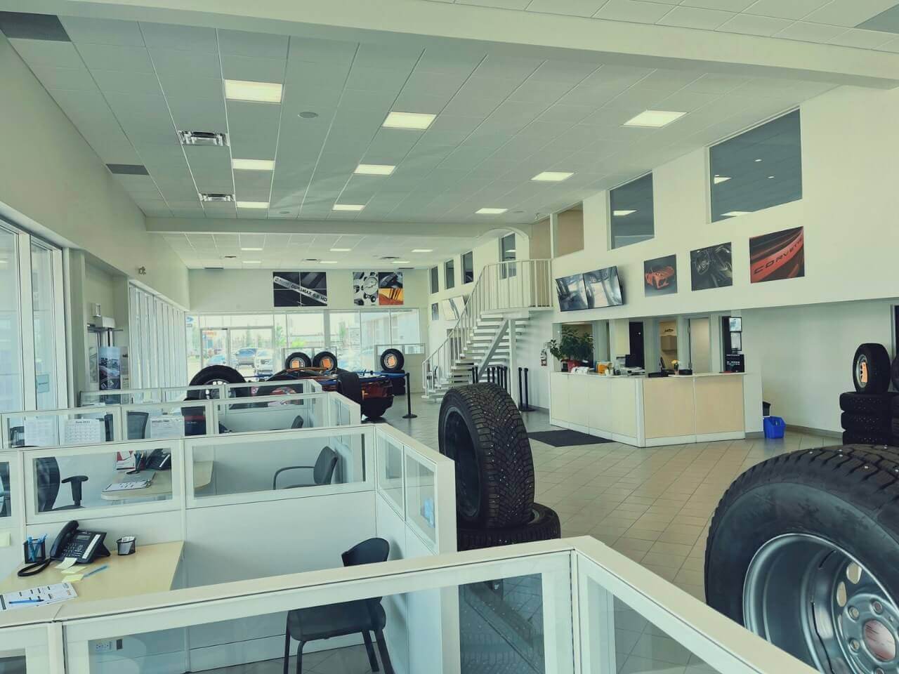 Car dealership interior with cubicles, tires, and reception desk. Bright, modern design.