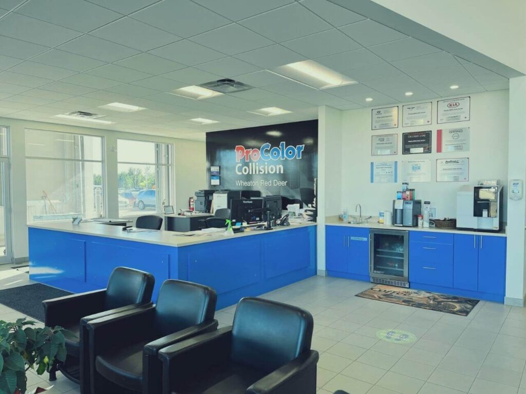Collision repair shop reception area with a blue counter, chairs, and framed certificates on the wall.