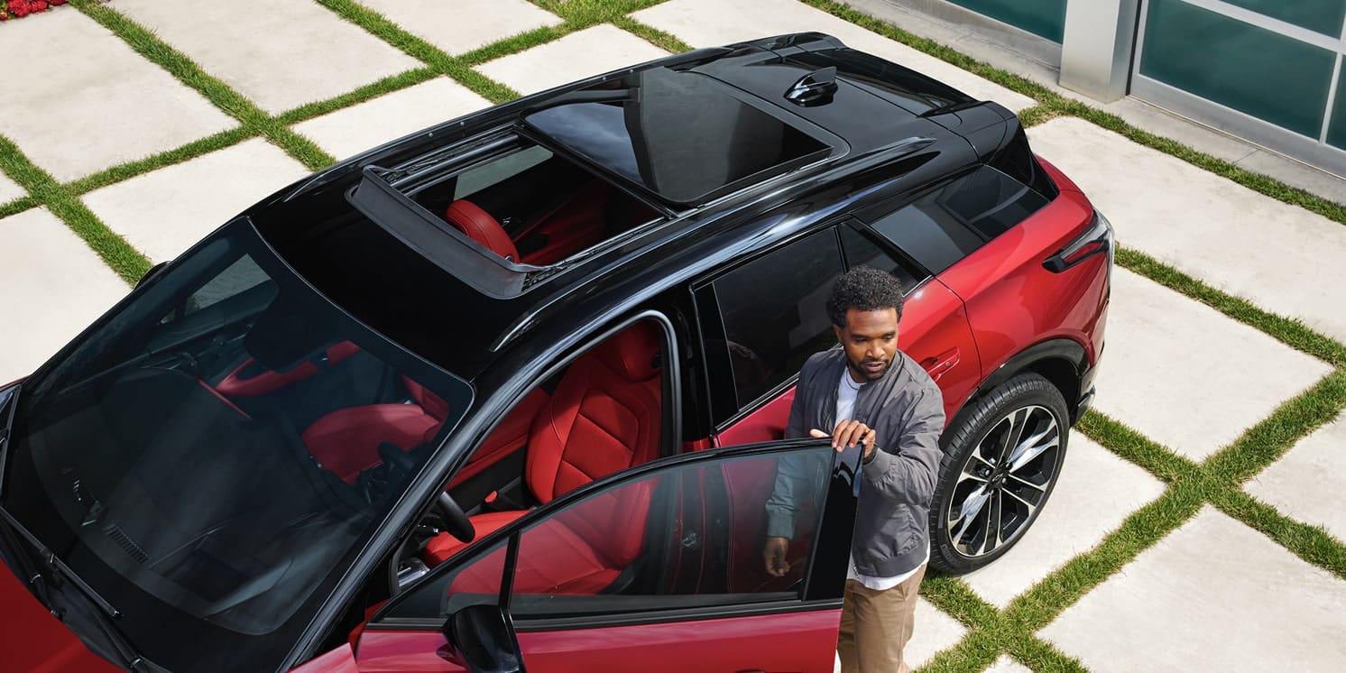 Man opening door of a red SUV with a panoramic sunroof and red interior, on a modern driveway.