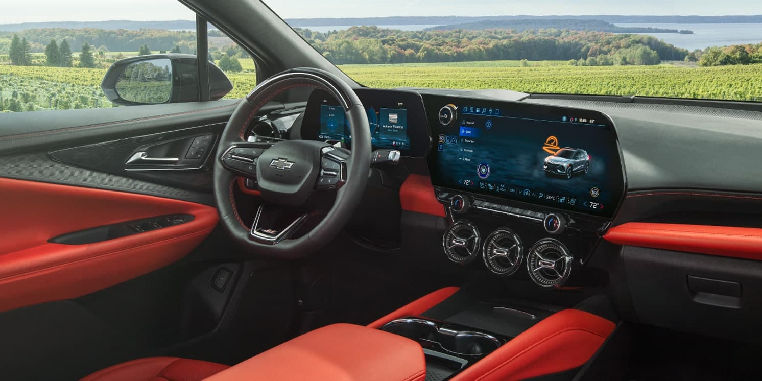 Modern car interior with red accents, digital displays, and vineyard view through the window.