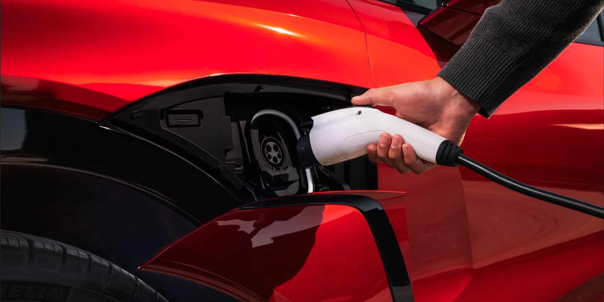 Charging an electric car with a white plug. Close-up of a red vehicle and a hand connecting the charger.