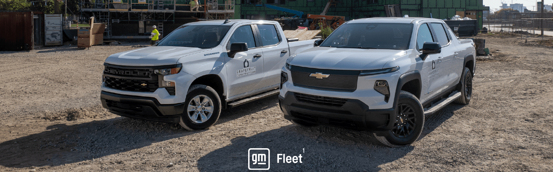 Two Chevrolet pickup trucks on a construction site with buildings and workers in the background.